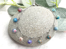 Load image into Gallery viewer, Bracelet with colorful lilac and blue sea sediment jasper stones on a stone surface with greenery in the background