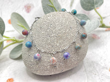 Load image into Gallery viewer, Bracelet with colorful lilac and blue sea sediment jasper stones  on a stone surface with greenery in the background
