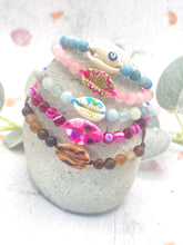 Load image into Gallery viewer, Colorful beaded bracelets with shell elements on a textured surface
